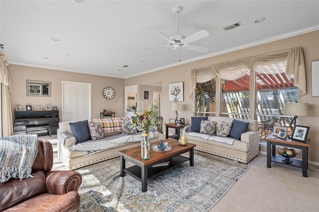 Flooded with natural light, this expansive living room offers stunning views of the lush golf course through a wall of floor-to-ceiling windows. The neutral color palette, plush carpeting, and elegant window treatments create a warm and inviting atmosphere, perfect for both relaxation and entertaining. | Image 13