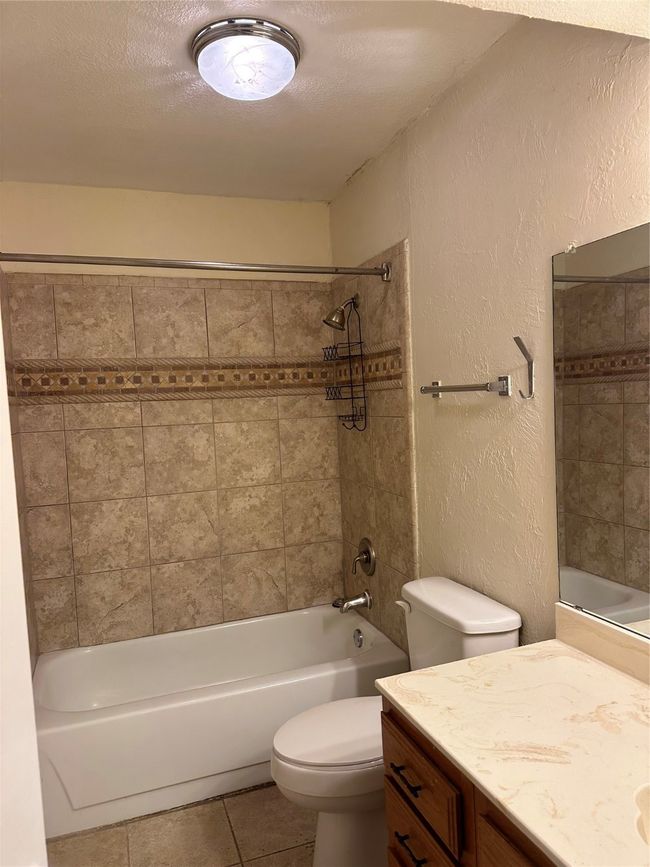 Full bathroom featuring vanity, a textured wall, tile patterned floors, tub / shower combination, and a textured ceiling | Image 4