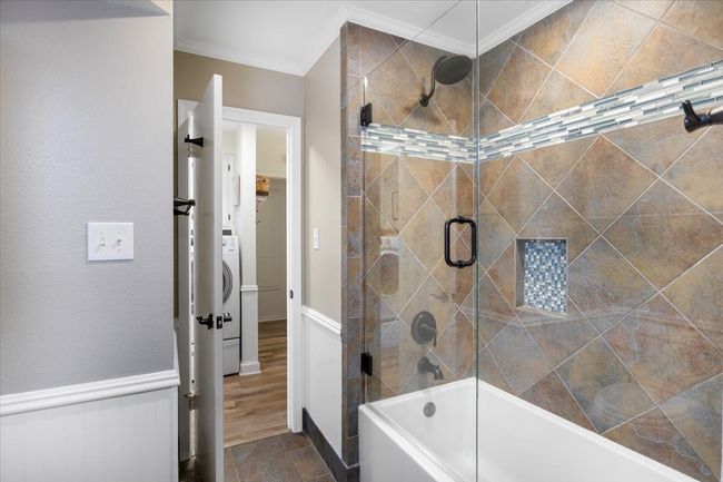 Full bath featuring enclosed tub / shower combo, washer / dryer, and crown molding | Image 24