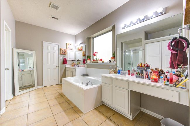 This spacious bathroom features a large soaking tub, dual vanities with ample counter space, and a walk-in shower. It has modern lighting, tile flooring, and a neutral color palette, creating a bright and inviting atmosphere. | Image 23