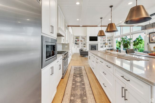 Kitchen with stainless steel appliances, open floor plan, light wood-style flooring, a fireplace, and white cabinetry | Image 25