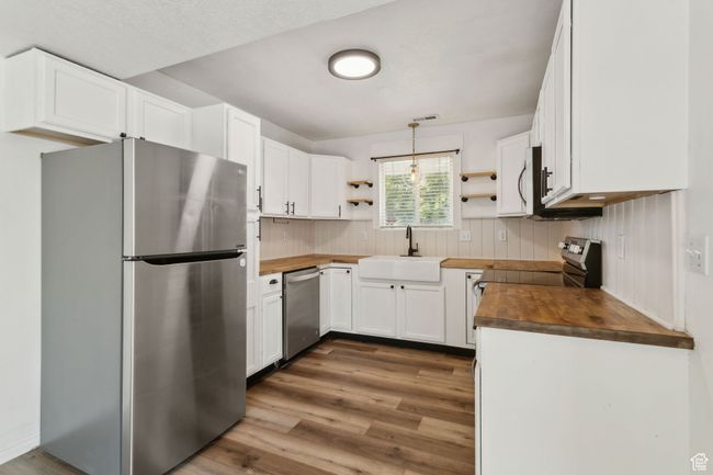Kitchen with appliances with stainless steel finishes, butcher block countertops, open shelves, and a sink | Image 4