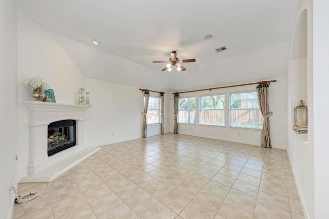 Unfurnished living room featuring a glass covered fireplace, light tile patterned floors, a ceiling fan, visible vents, and lofted ceiling | Image 12