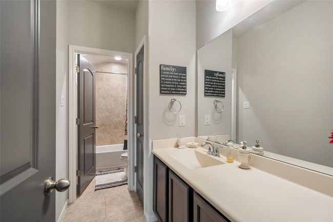 The secondary downstairs bathroom features a modern design with a large mirror and double sink vanity. It has a neutral color palette and leads into a tiled bathtub and shower area. | Image 23