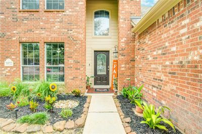 Stroll down the inviting walkway featuring fresh landscaping leading to a beautiful wooden door with leaded glass, set within an impressive two-story entryway. | Image 2