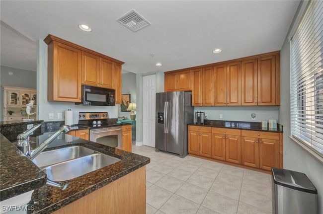Kitchen featuring stainless steel appliances, recessed lighting, light tile patterned floors, dark stone countertops, and brown cabinets | Image 16