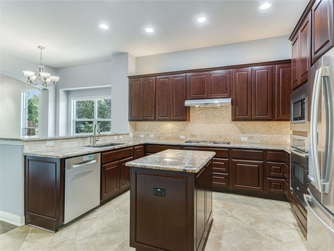 Enjoy granite counters, a center island, ample cabinet storage with lighting, and stainless appliances. | Image 7