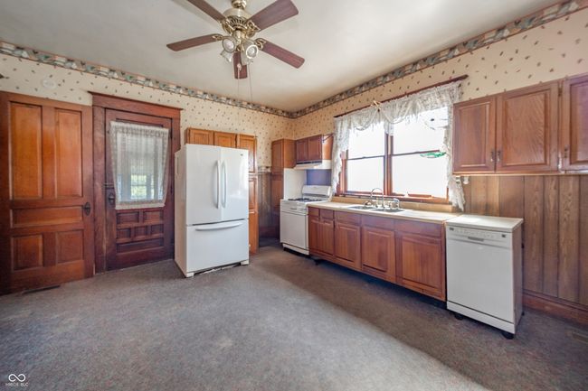 kitchen featuring white appliances, a sink, wallpapered walls, and brown cabinets | Image 8