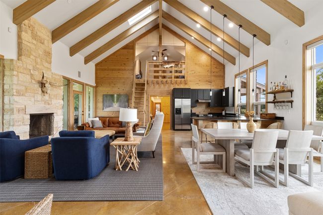 Living area featuring high vaulted ceiling, wooden walls, a fireplace, beam ceiling, and finished concrete flooring | Image 15