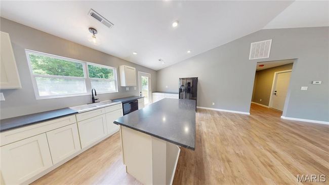 Kitchen with a sink, vaulted ceiling, dark countertops, light wood finished floors, and white cabinetry | Image 12