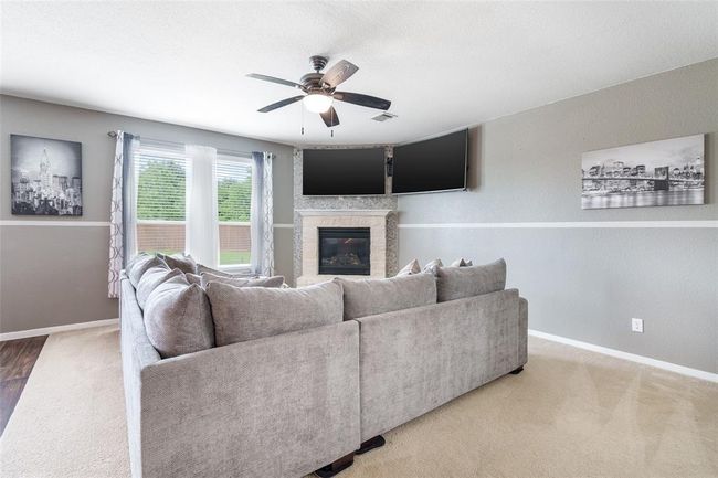 The living room features a charming fireplace, plush carpet flooring, and multiple windows with privacy blinds that fill the space with natural light. | Image 4