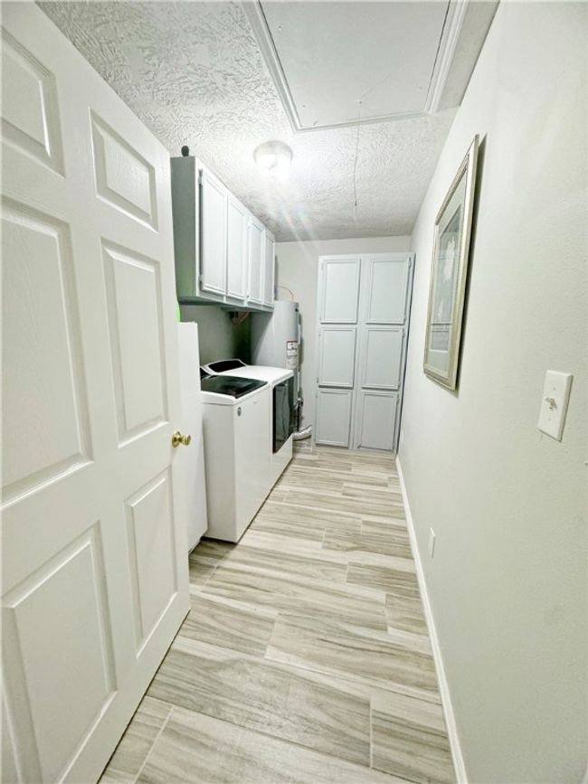 Washroom with a textured ceiling, attic access, separate washer and dryer, cabinet space, and baseboards | Image 14
