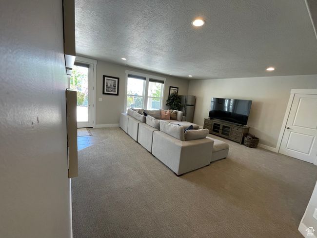 Basement living room featuring natural light, walkout basement door, light carpet, and recessed lighting | Image 43