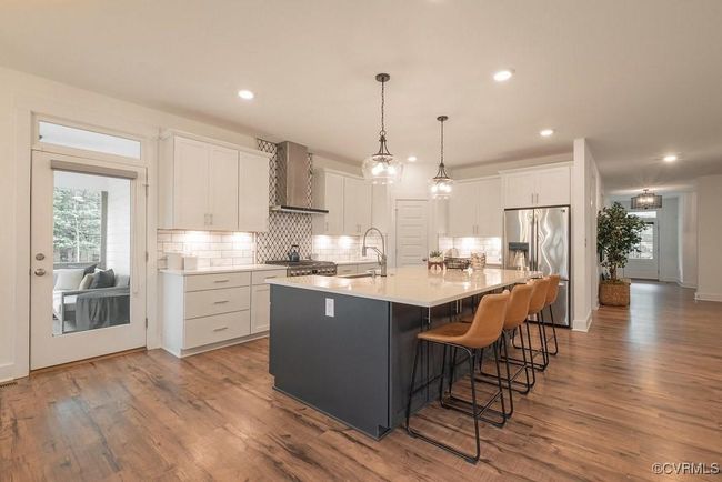 Kitchen featuring a center island with sink, stainless steel fridge, white cabinetry, wall chimney exhaust hood, and tasteful backsplash | Image 26