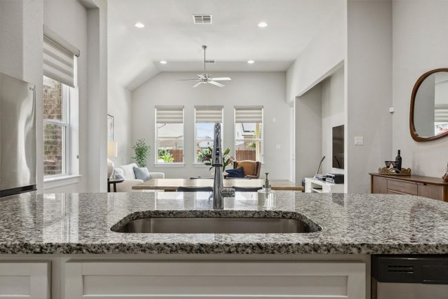 Kitchen with open floor plan, light stone counters, stainless steel dishwasher and gleaming white cabinets | Image 9
