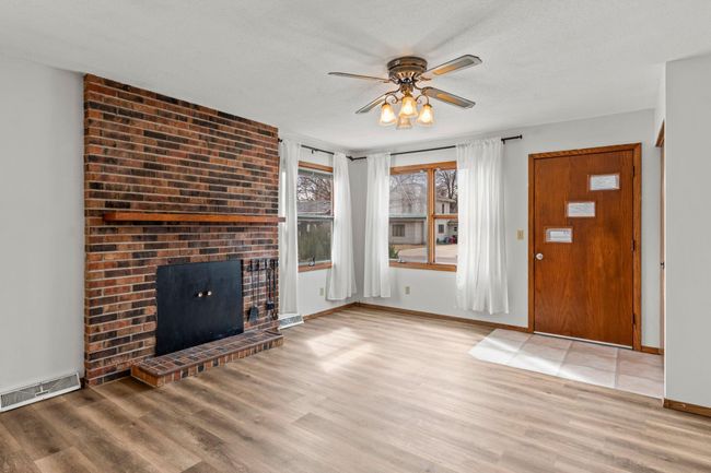 The living room, situated adjacent to the kitchen, boasts a wood-burning fireplace with a mantel and brick surround, durable LVP flooring, and a ceiling fan. | Image 4