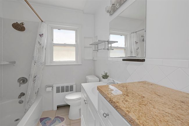 Full bath with radiator, toilet, vanity, shower / bath combination with curtain, and tile patterned floors | Image 12