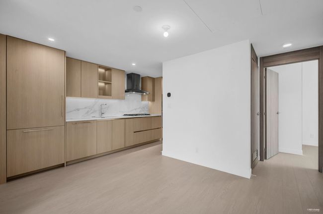 Kitchen with wall chimney exhaust hood, light wood-style flooring, light countertops, decorative backsplash, and light brown cabinetry | Image 7