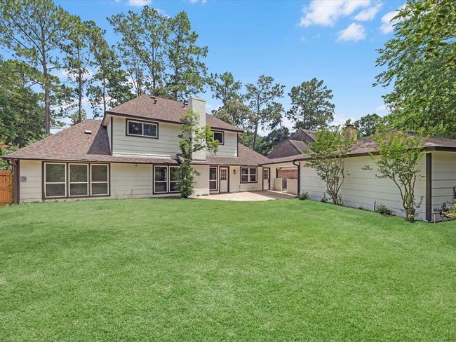 This photo shows a spacious backyard with a well-maintained lawn and a two-story house featuring a mix of light-colored siding and windows. The property is surrounded by mature trees, offering privacy and a natural setting. | Image 36