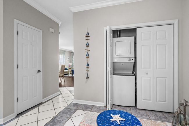 Laundry area featuring estacked washer and dryer, ornamental molding, light tile patterned flooring, and baseboards | Image 30