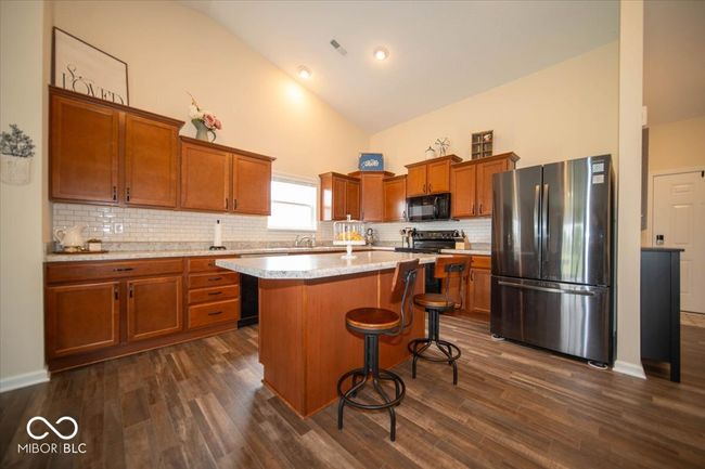kitchen with freestanding refrigerator, black microwave, high vaulted ceiling, a breakfast bar, and brown cabinetry | Image 13