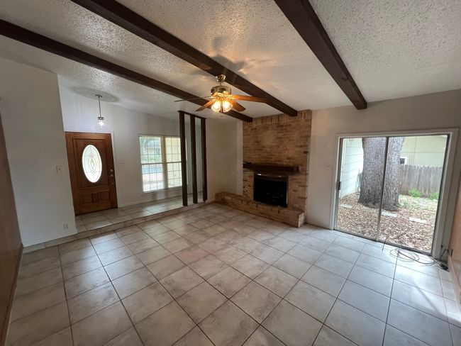 Unfurnished living room with light tile patterned floors, beamed ceiling, a ceiling fan, a textured ceiling, and a fireplace | Image 5