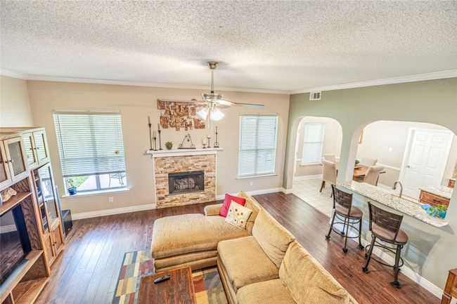 Living room featuring a fireplace, arched walkways, a textured ceiling, wood-type flooring, and crown molding | Image 11