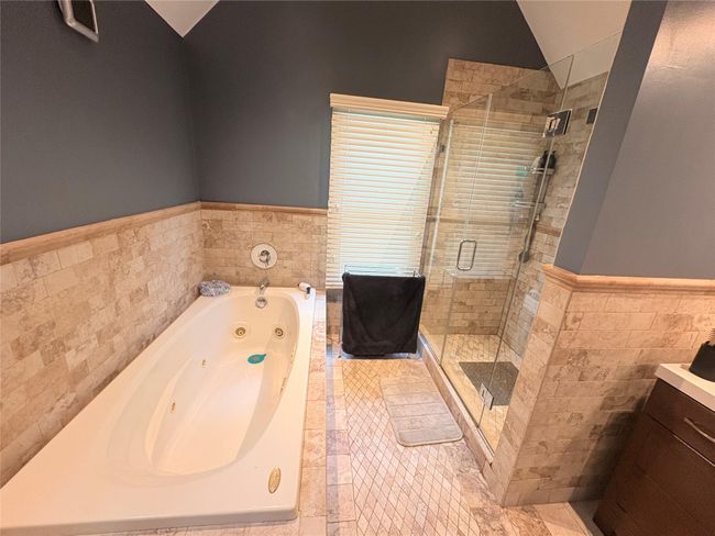 Bathroom featuring tile walls, a shower stall, a tub with jets, wainscoting, and vaulted ceiling | Image 12
