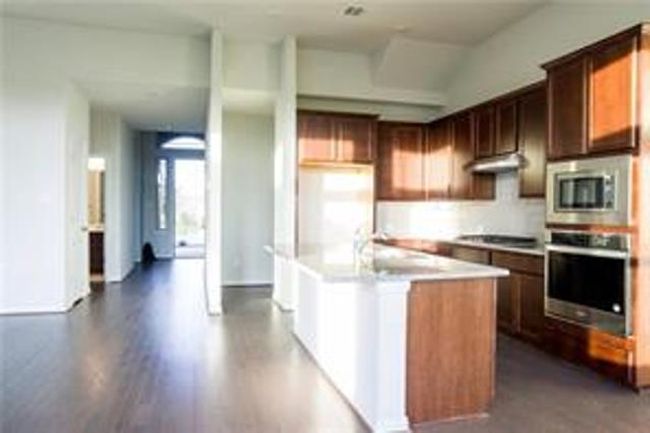 Kitchen featuring stainless steel appliances, light countertops, a kitchen island with sink, dark wood finished floors, and under cabinet range hood | Image 5