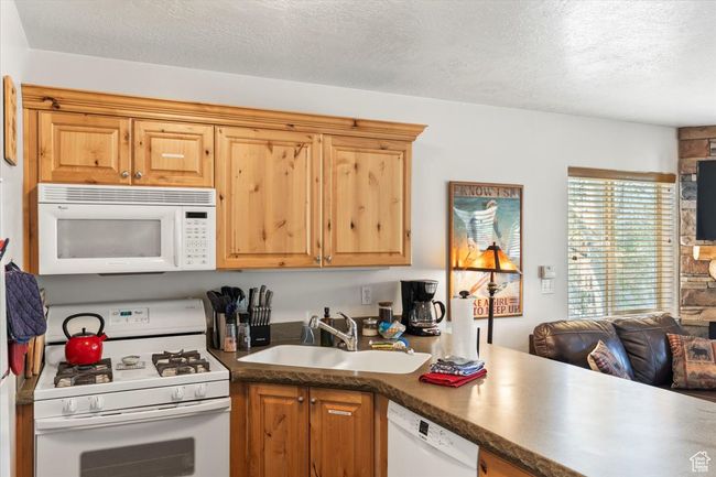 Kitchen featuring a sink, a textured ceiling, white appliances, and dark countertops | Image 5