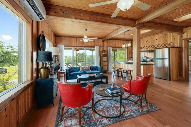 Living room featuring a ceiling fan, wood finished floors, a wall mounted AC, wooden walls, and beamed ceiling | Image 5