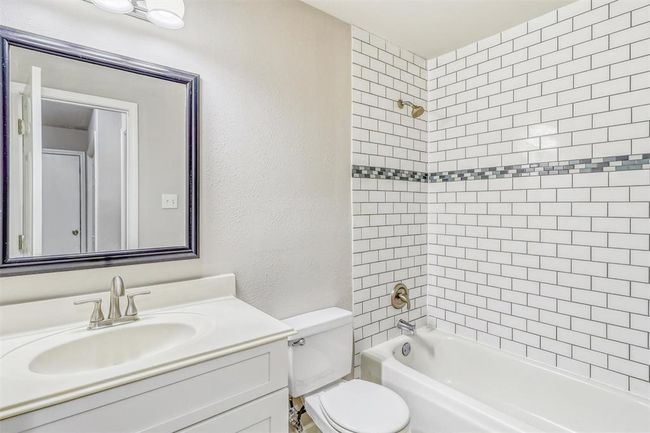 Guests will appreciate the updated bathroom, featuring a sleek shower/tub combo with a full-height subway tile surround and a stylish accent inlay for added depth. The vanity offers shaker-style cabinetry and brushed nickel finishes for a polished touch. | Image 27