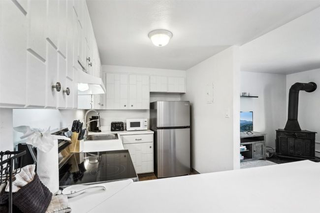 Kitchen featuring a sink, white microwave, light countertops, white cabinetry, and freestanding refrigerator | Image 12