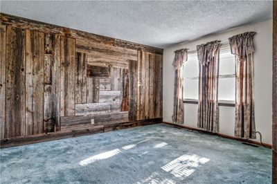 Carpeted living room with a textured ceiling and barn wood wall | Image 2