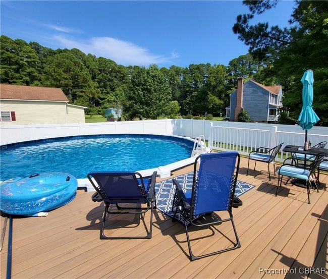 View of swimming pool with fence, a wooden deck, outdoor dining area, and a view of trees | Image 33