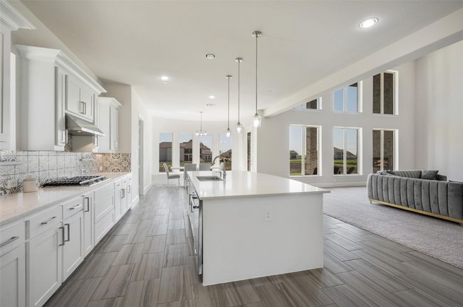Kitchen with light countertops, open floor plan, white cabinets, a sink, and under cabinet range hood | Image 8