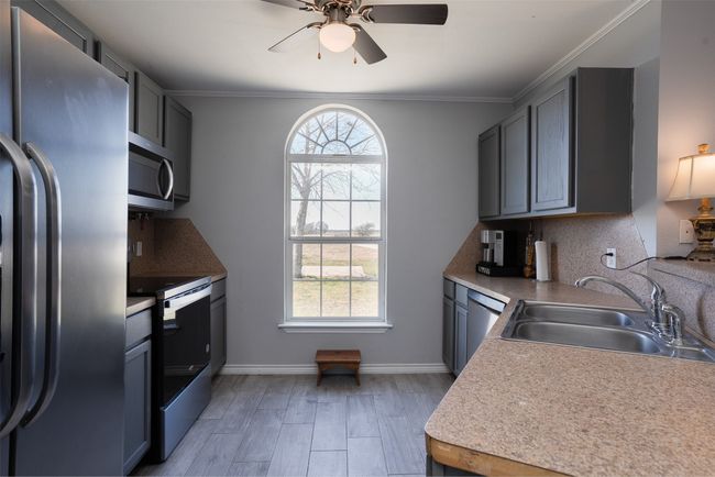 Kitchen featuring appliances with stainless steel finishes, a sink, a ceiling fan, light wood-type flooring, and baseboards | Image 11