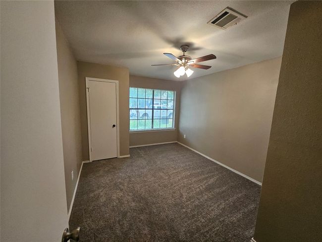 Unfurnished room with a textured ceiling, visible vents, baseboards, ceiling fan, and dark colored carpet | Image 5