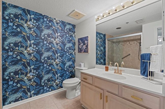 The guest bathroom is nicely appointed with a tiled shower, large vanity and accent wall with cheerful wallpaper. | Image 26