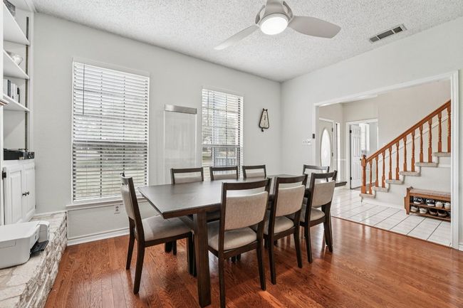 Dining area with a textured ceiling, wood finished floors, healthy amount of natural light, ceiling fan, and stairway | Image 9