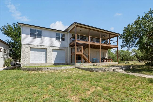 Back of property featuring stairs, an attached garage door that opens to a large unfinished area, a lawn, and ceiling fan | Image 29