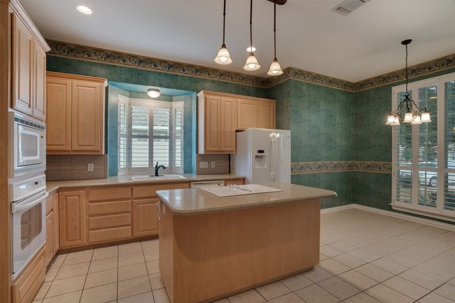 Kitchen with white appliances, wallpapered walls, a sink, light tile patterned floors, and light brown cabinets | Image 10