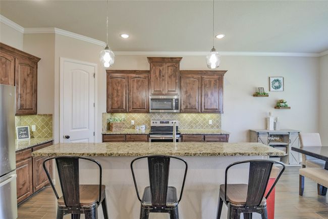 Kitchen featuring stainless steel appliances, a kitchen bar, ornamental molding, and wood finished floors | Image 13