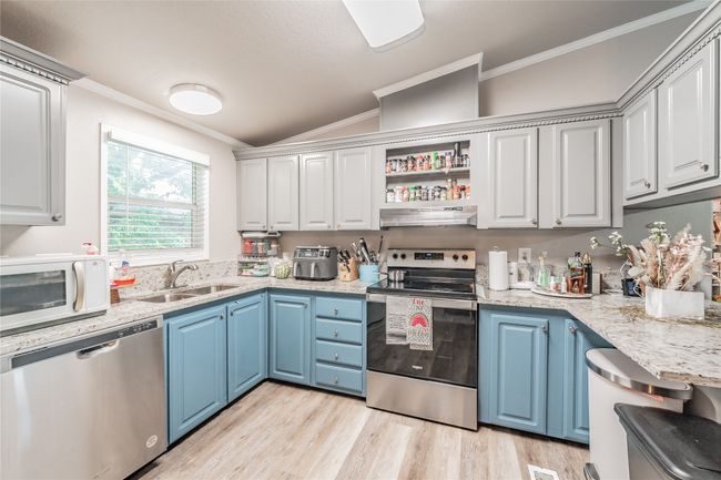 Kitchen featuring stainless steel appliances, ornamental molding, under cabinet range hood, blue cabinetry, and light wood-type flooring | Image 13