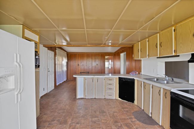 Kitchen with dishwasher, white fridge with ice dispenser, a sink, a peninsula, and wood walls | Image 12