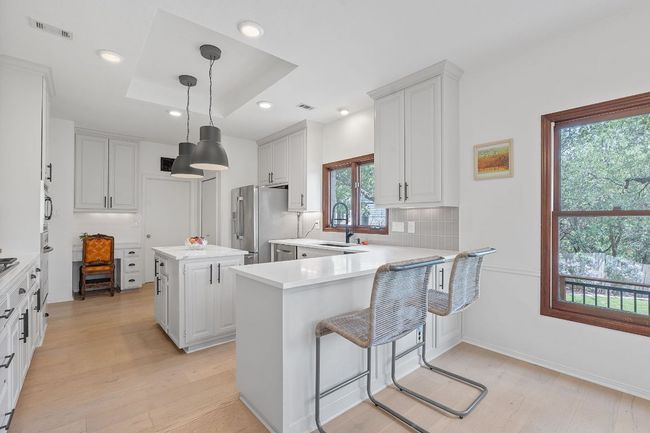 Kitchen with stainless steel fridge with ice dispenser, light wood-type flooring, light countertops, a kitchen island, and a peninsula | Image 9