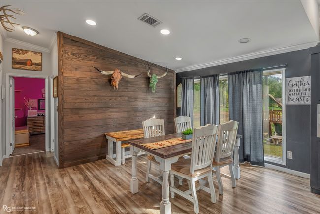 Dining room with wood walls, visible vents, baseboards, ornamental molding, and wood finished floors | Image 17