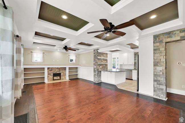 Unfurnished living room featuring a fireplace with flush hearth, crown molding, ceiling fan, and coffered ceiling | Image 4