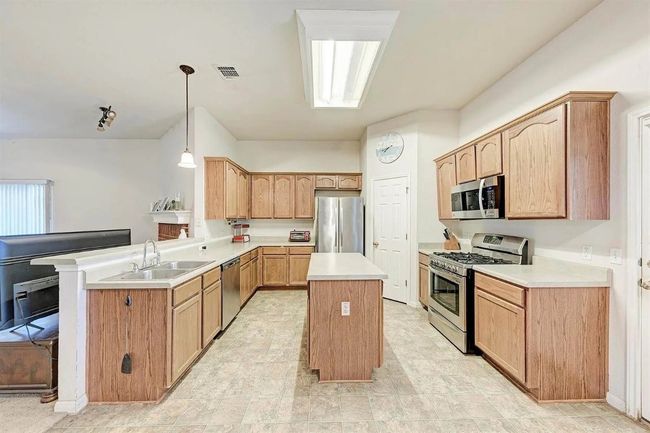 Kitchen featuring stainless steel appliances, a kitchen island, light countertops, a peninsula, and hanging light fixtures | Image 13