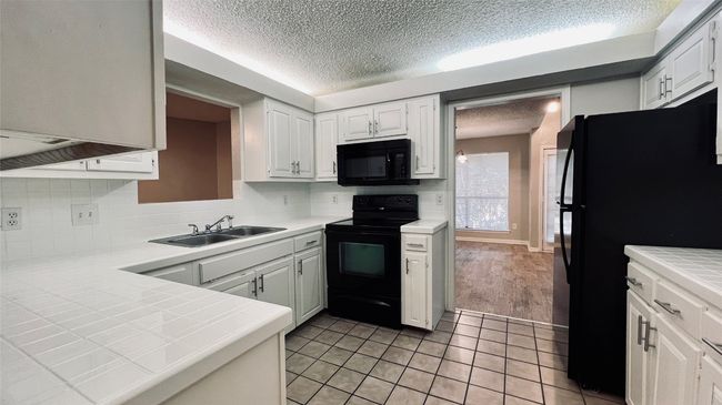 Kitchen featuring black appliances, a sink, a textured ceiling, tile countertops, and light tile patterned flooring | Image 4